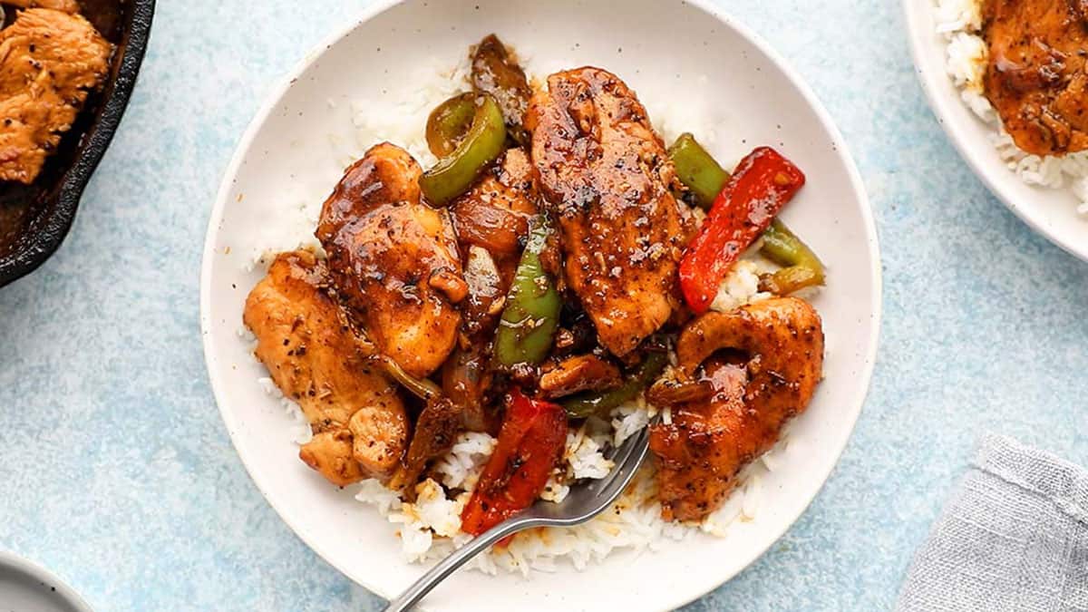 black pepper chicken stir fry with white rice in a white bowl and a metal fork.