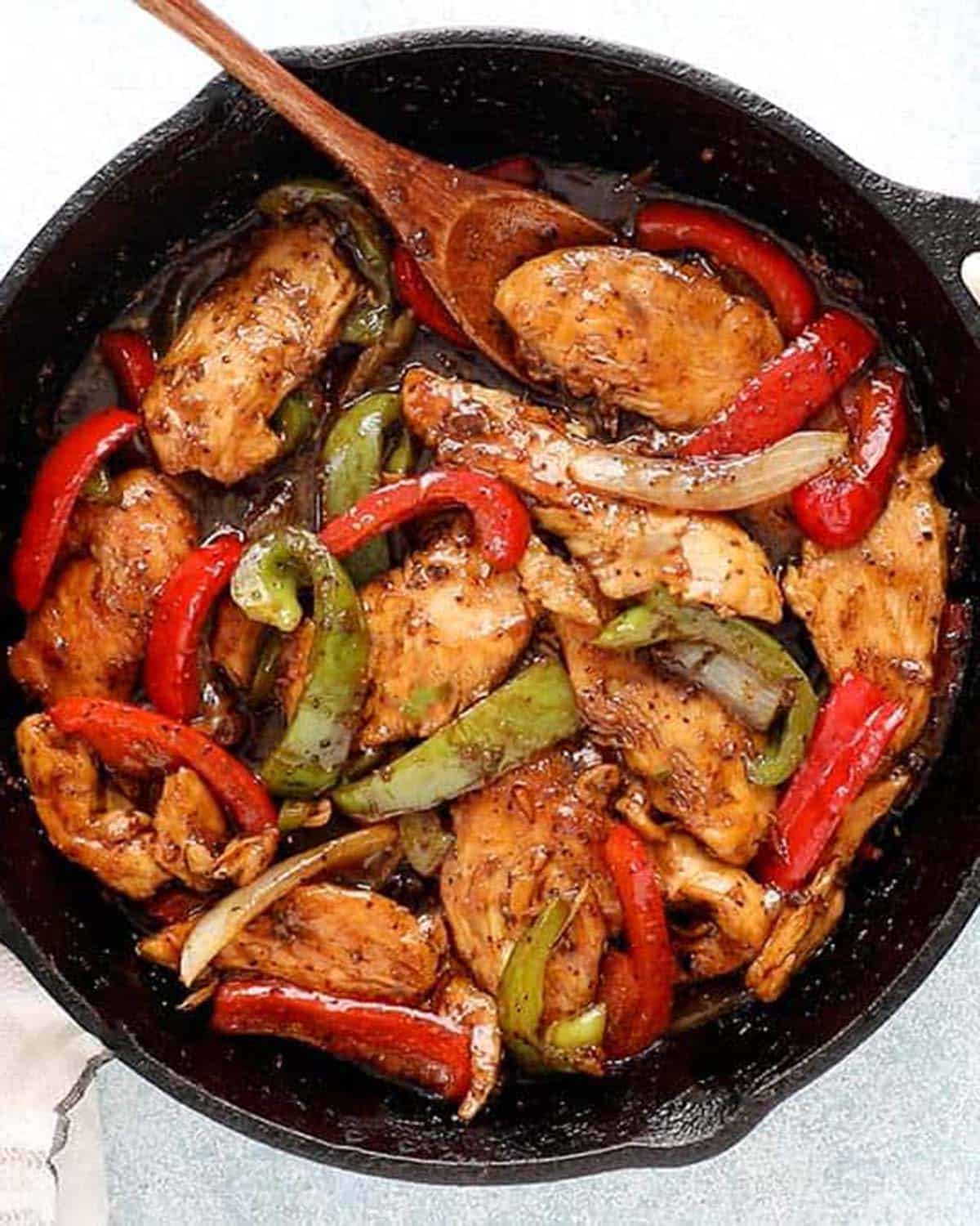 cooked black pepper chicken stir fry in a black skillet placed on a stove.
