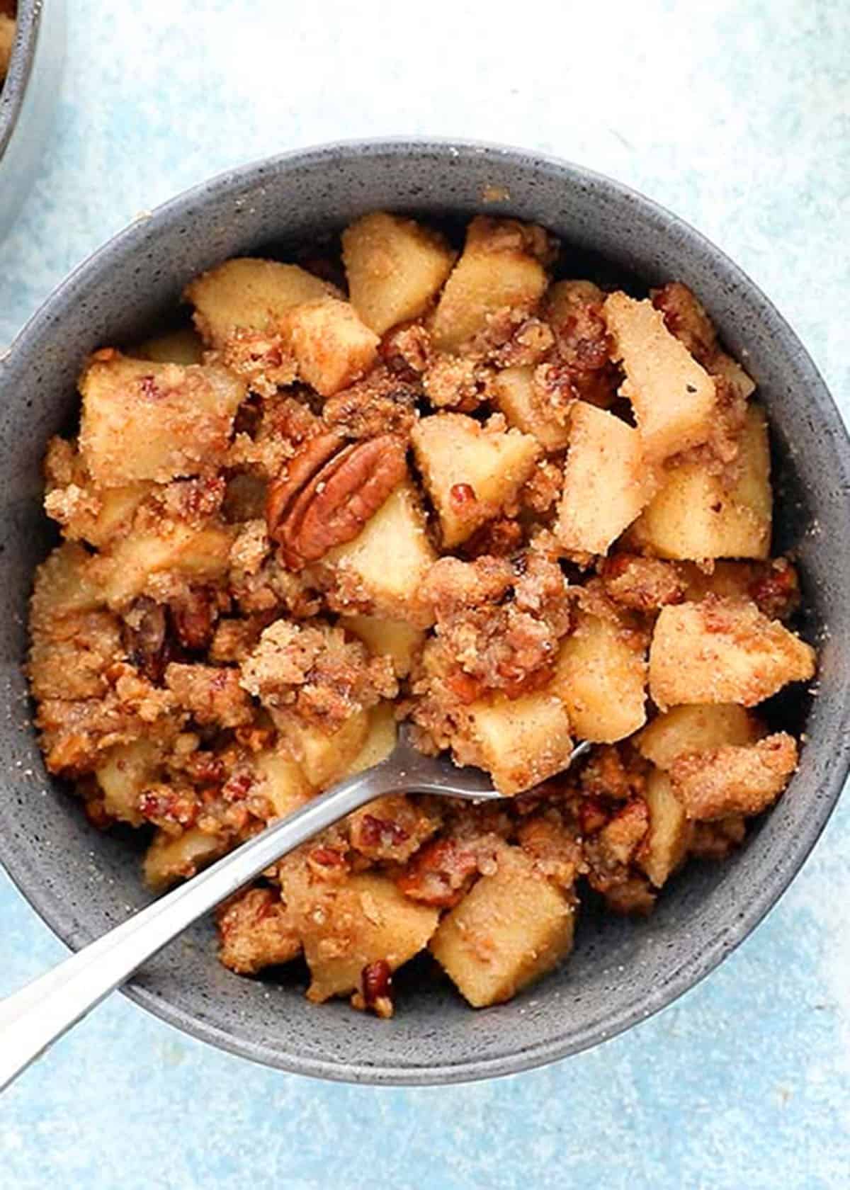 baked apple crumble in a blue bowl along with a spoon.