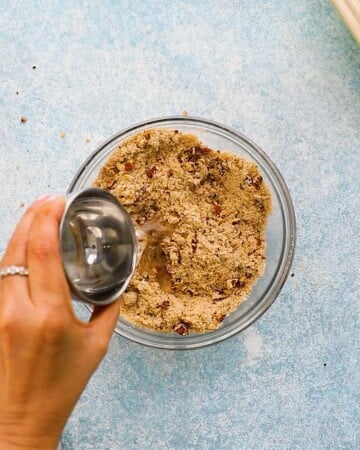 a hand pouring melted coconut oil into a small glass bowl.