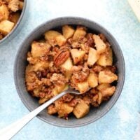 apple crumble in a blue colored bowl along with one spoon.