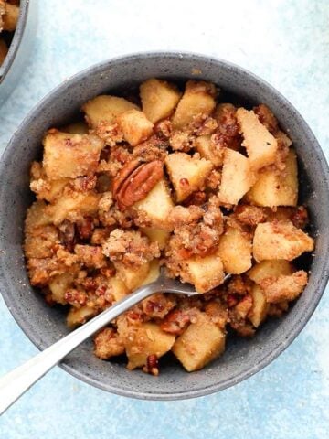 apple crumble in a blue colored bowl along with one spoon.