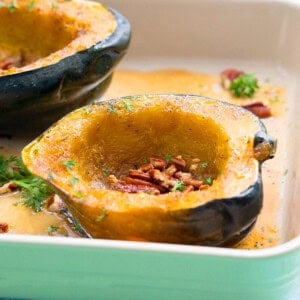 two cut acorn squash halves in a green baking dish.