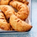 apple hand pies placed on a parchment lined white metal tray.