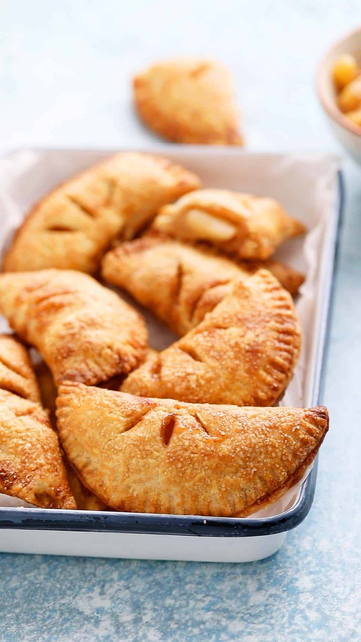 apple hand pies placed on a parchment lined white metal tray.