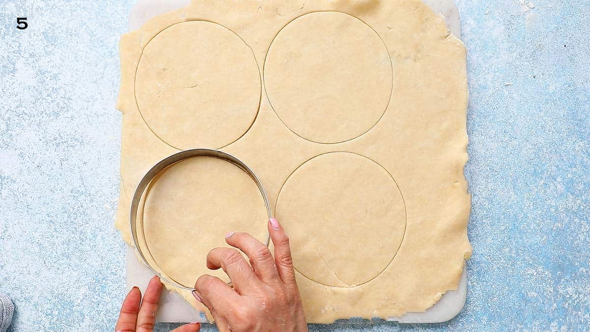 two hand cutting circles using a round metal cookie cutter from rolled pie crust.