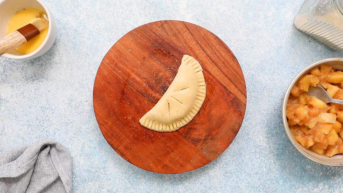 one shaped apple hand pie placed on a round wooden cutting board.