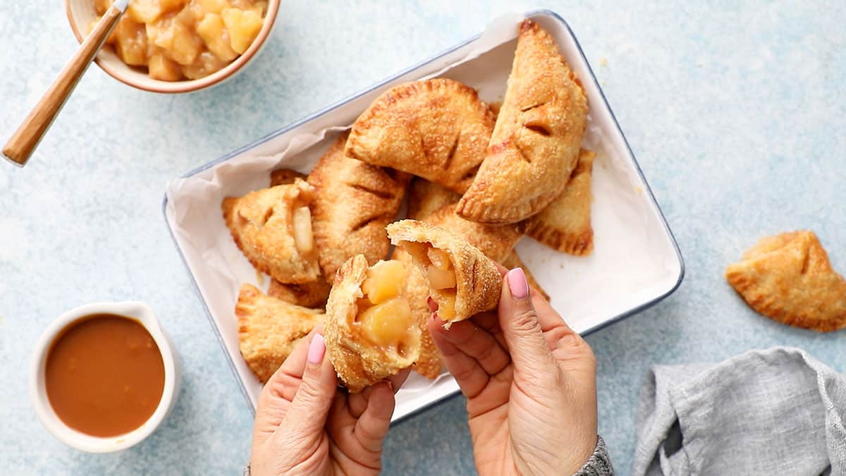 two hands breaking open an apple hand pie.