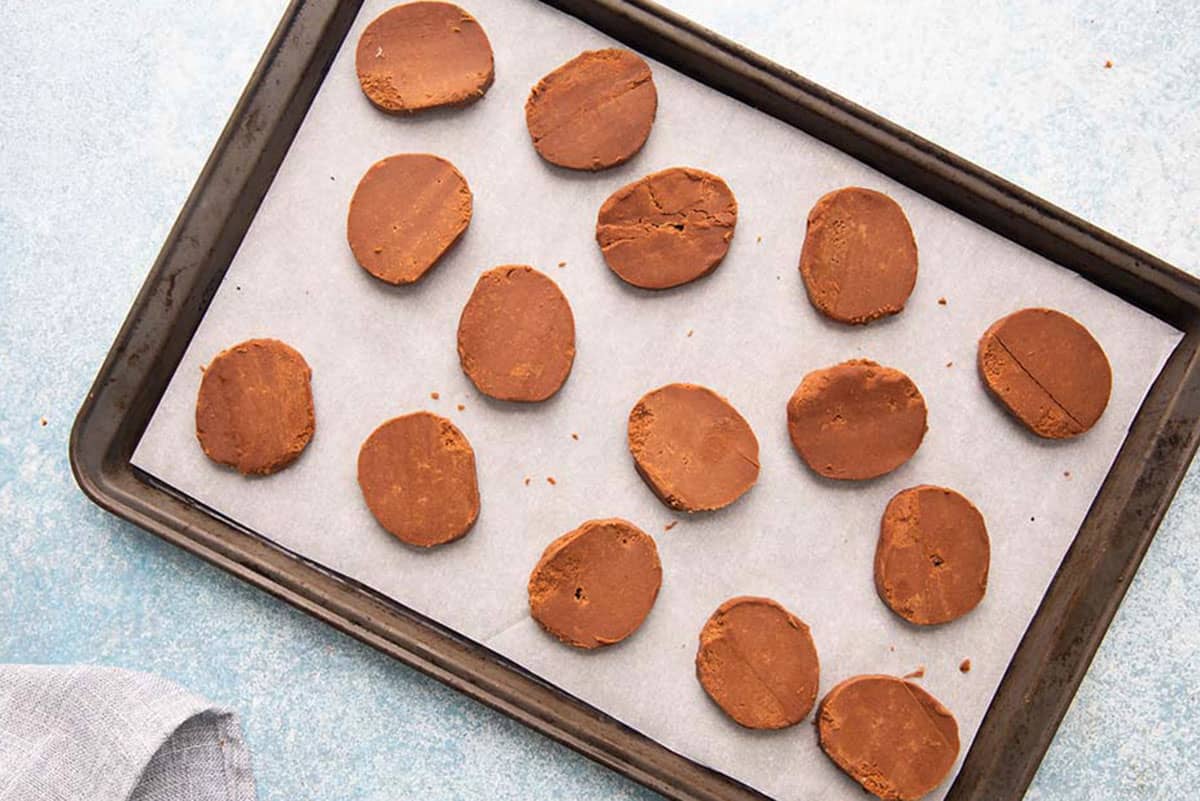 brown cookie dough sliced placed on a parchment lined baking sheet.