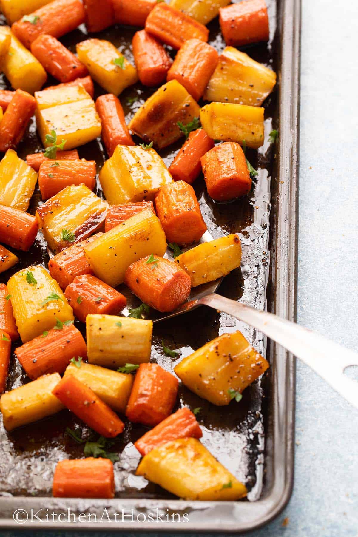 roasted carrots and parsnips in a black baking sheet.