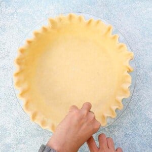 two hands making a fluted edge on a pie crust.