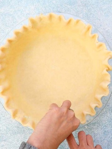 two hands making a fluted edge on a pie crust.