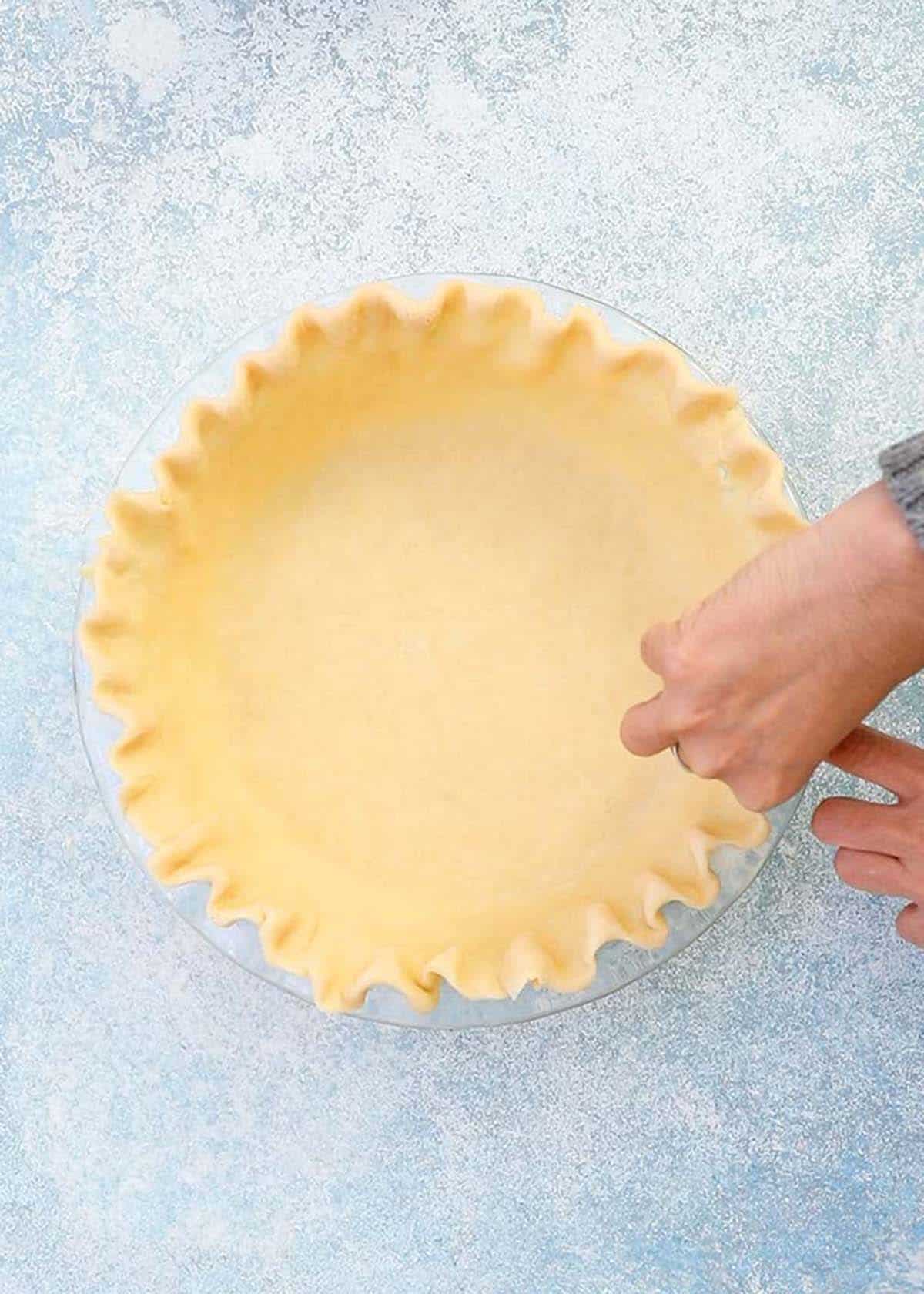 two hands shaping a fluted edge on a pie crust. 