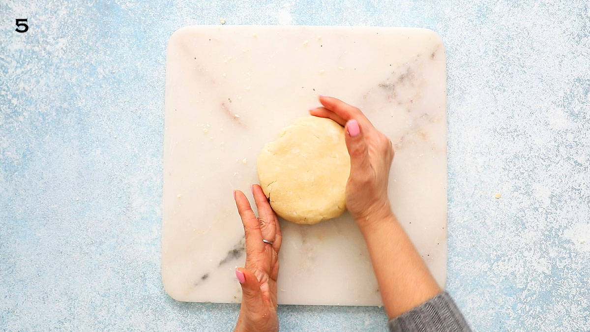 two hands shaping a pie crust disc on a square white marble board. 