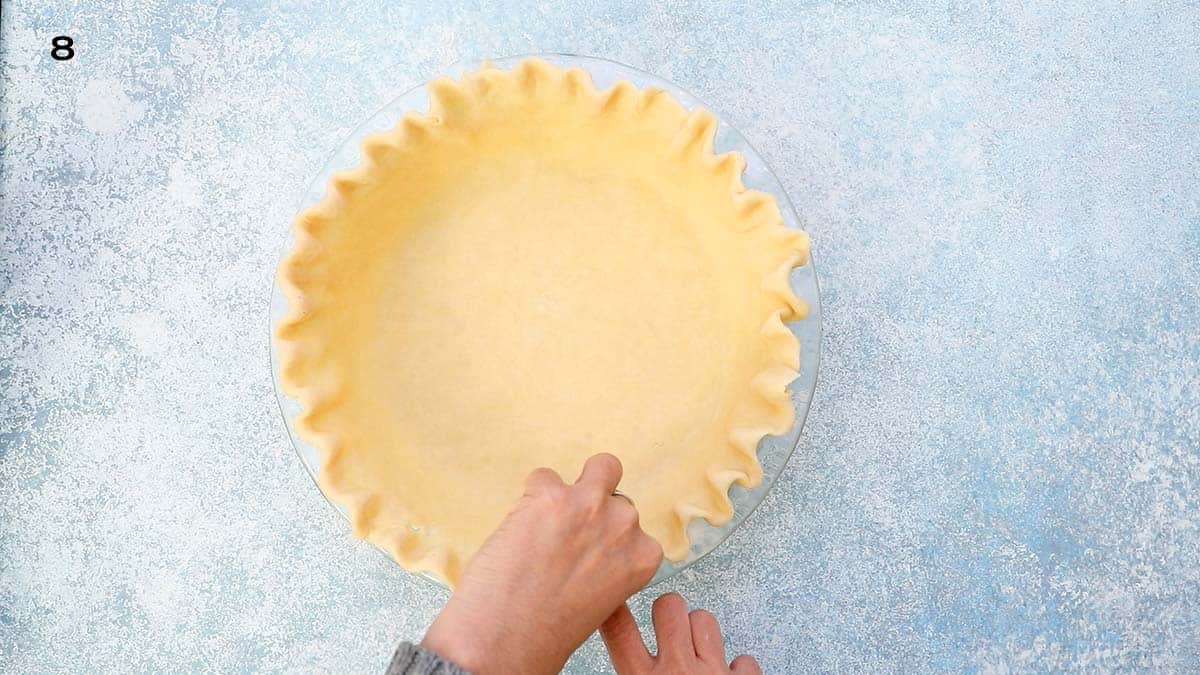 two hands shaping a fluted edge on a pie crust. 
