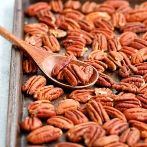 black baking sheet filled with toasted pecans along with a wooden spoon.