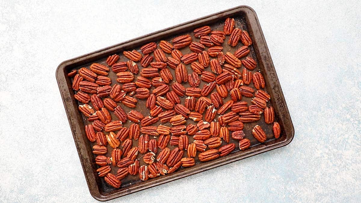 a black baking sheet filled with toasted pecans.