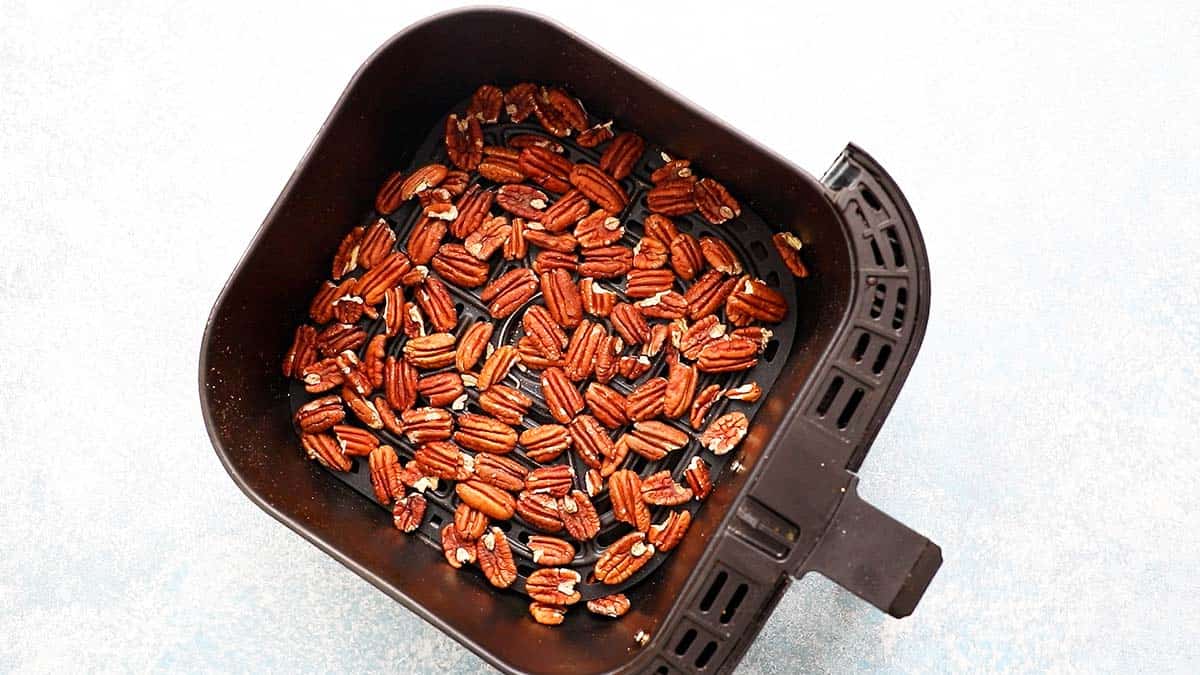 an air fryer basket filled with toasted pecans.