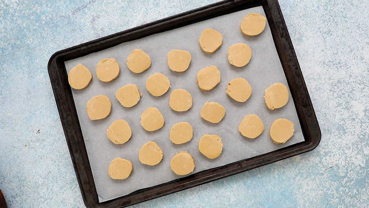 round raw cookie dough slices placed on a parchment lined baking sheet.