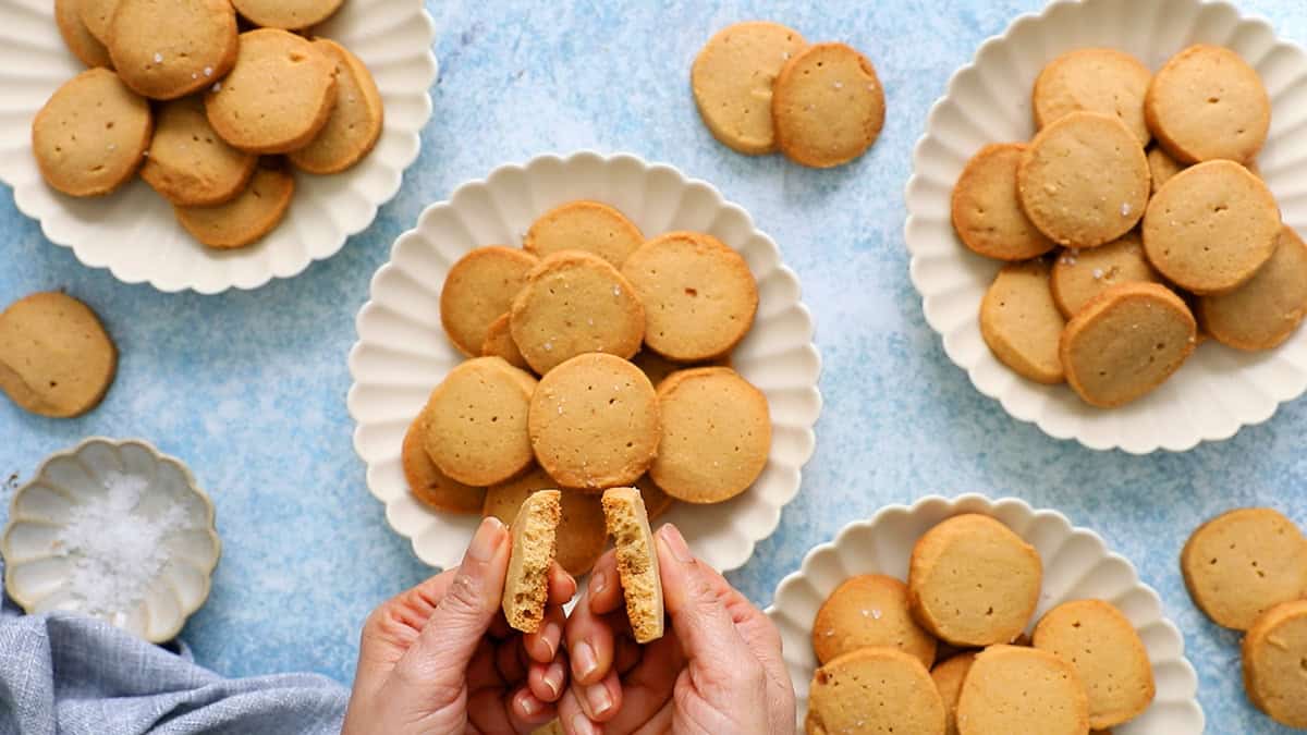 two hands holding each half of a broken brown sugar cookie.