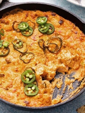 yellow colored buffalo chicken dip in a black skillet.