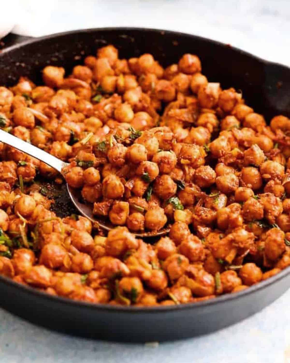 spicy cooked chickpeas in a black skillet.
