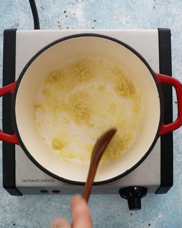 a hand cooking grated garlic in butter in a white pot.