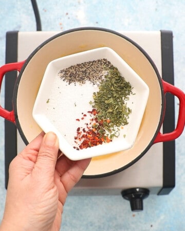 a hand holding a small white plate with red and green colored spices.