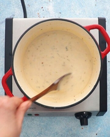 a hand cooking white sauce in a white pot.