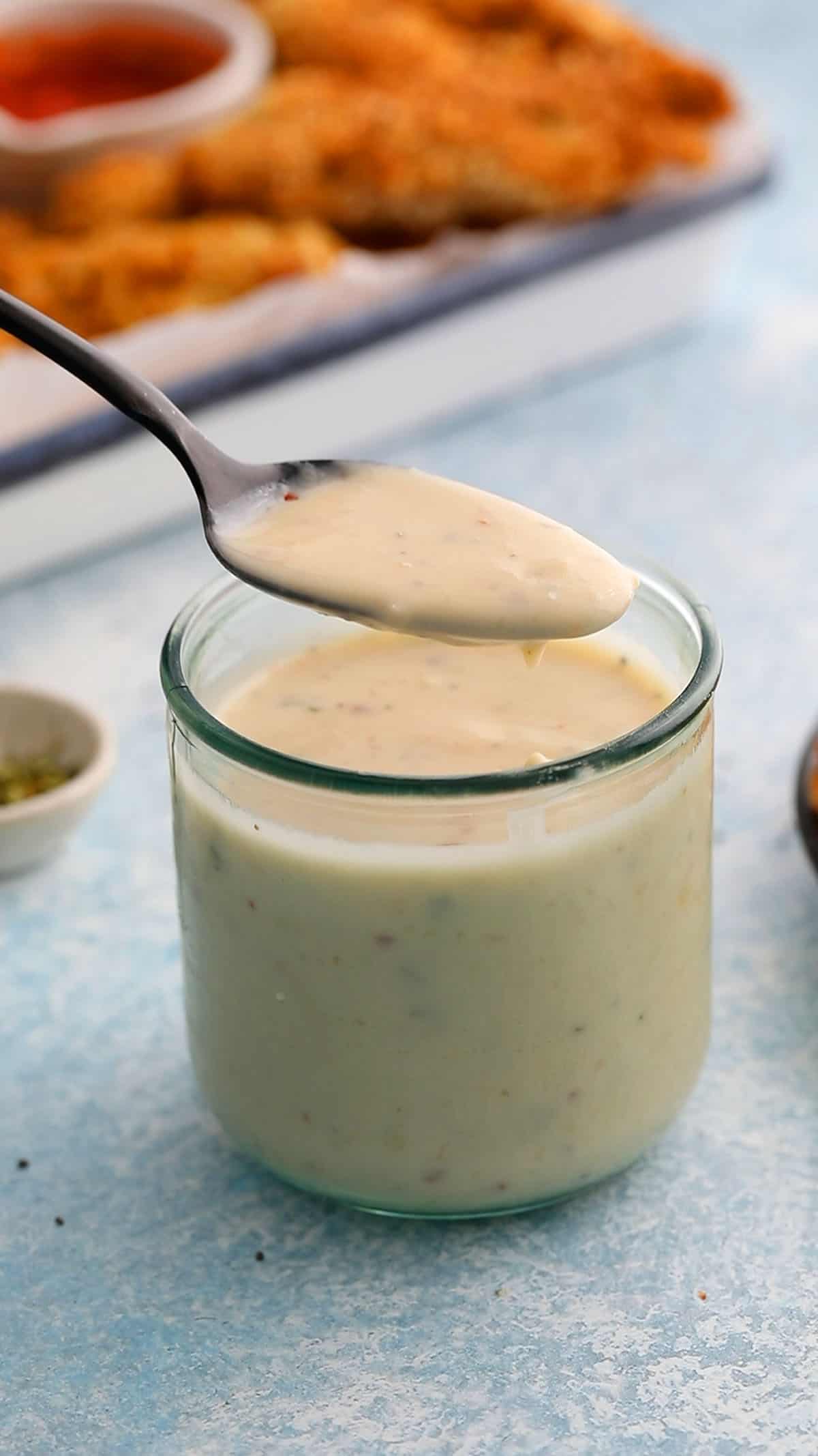 a spoonful of white sauce above a glass jar filled with the same.