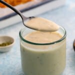 a spoonful of white sauce over a glass jar filled with the same.