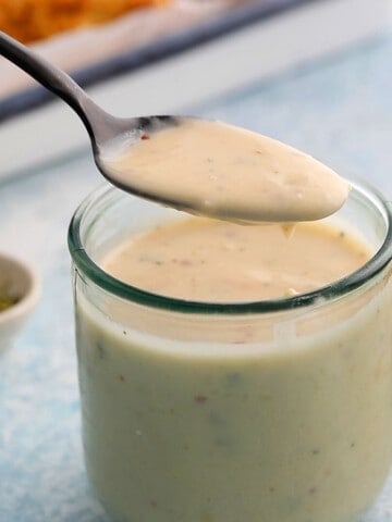 a spoonful of white sauce over a glass jar filled with the same.