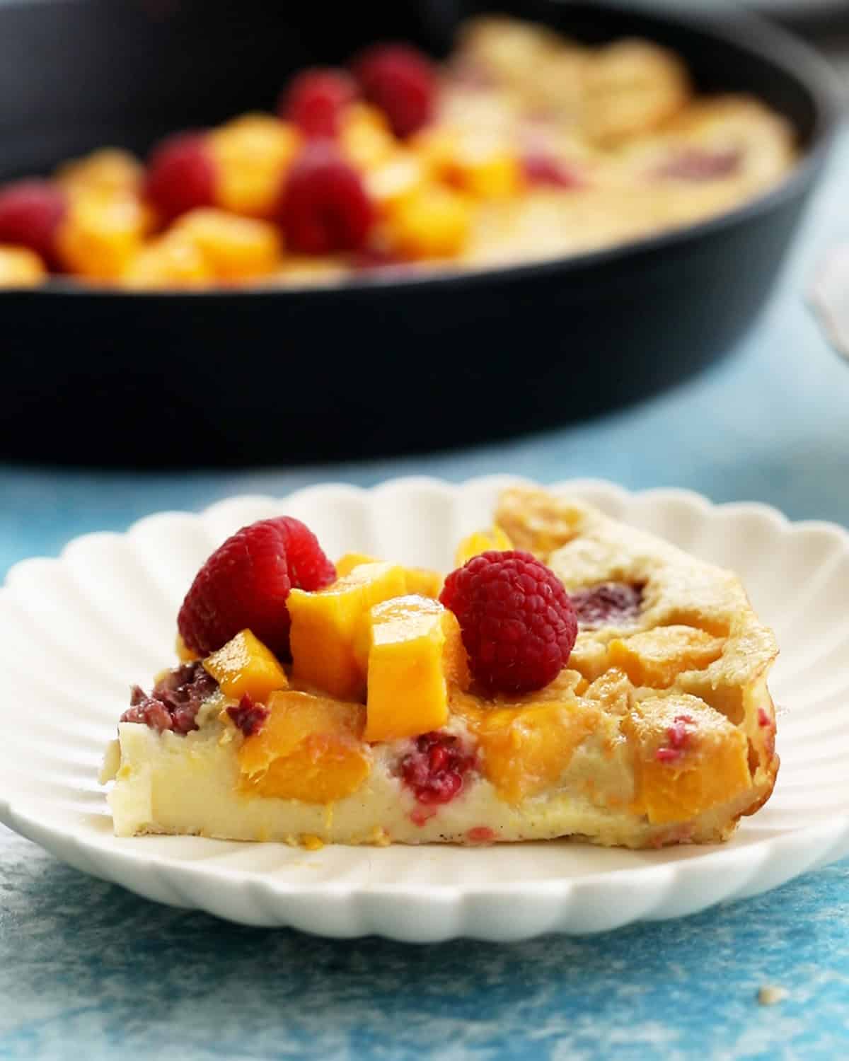 one slice of yellow clafoutis with pink raspberries in a white plate.
