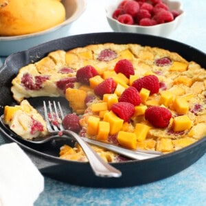 yellow mango clafoutis with pink raspberries in a black skillet.