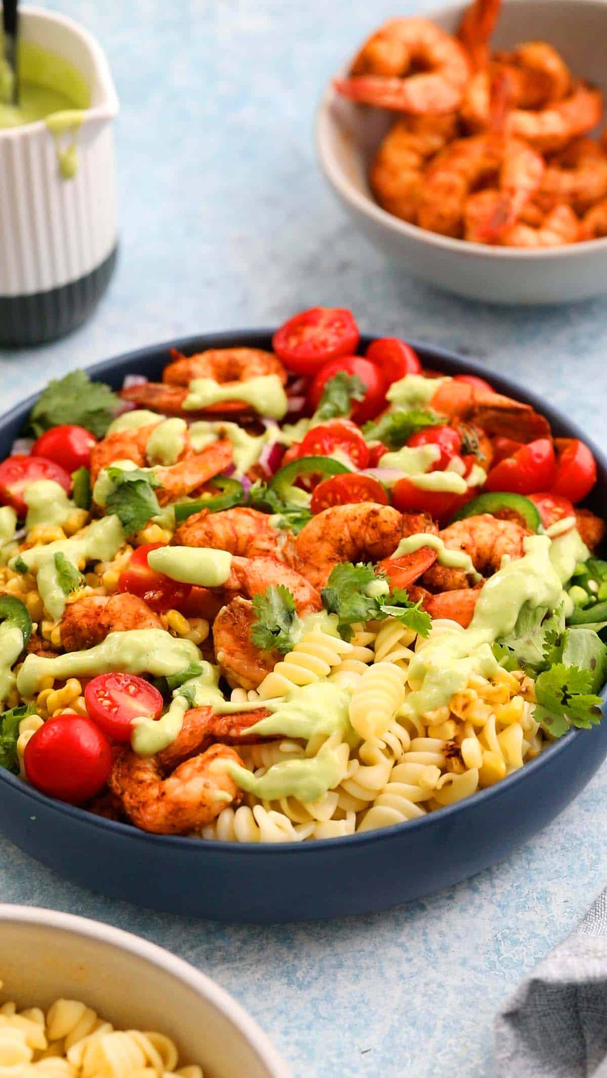 assembled shrimp and pasta salad, topped with green dressing in a blue bowl.