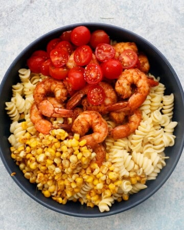 cooked pasta, shrimp, corn and tomatoes in a large blue bowl.
