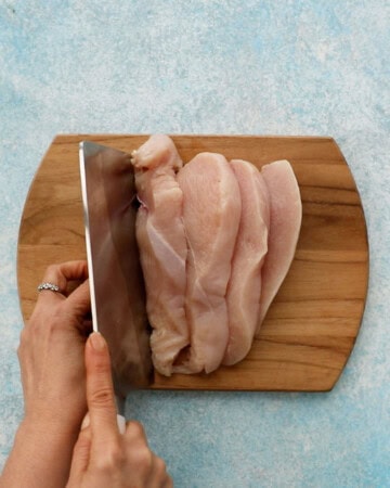 two hands cutting one chicken breast into nuggets.