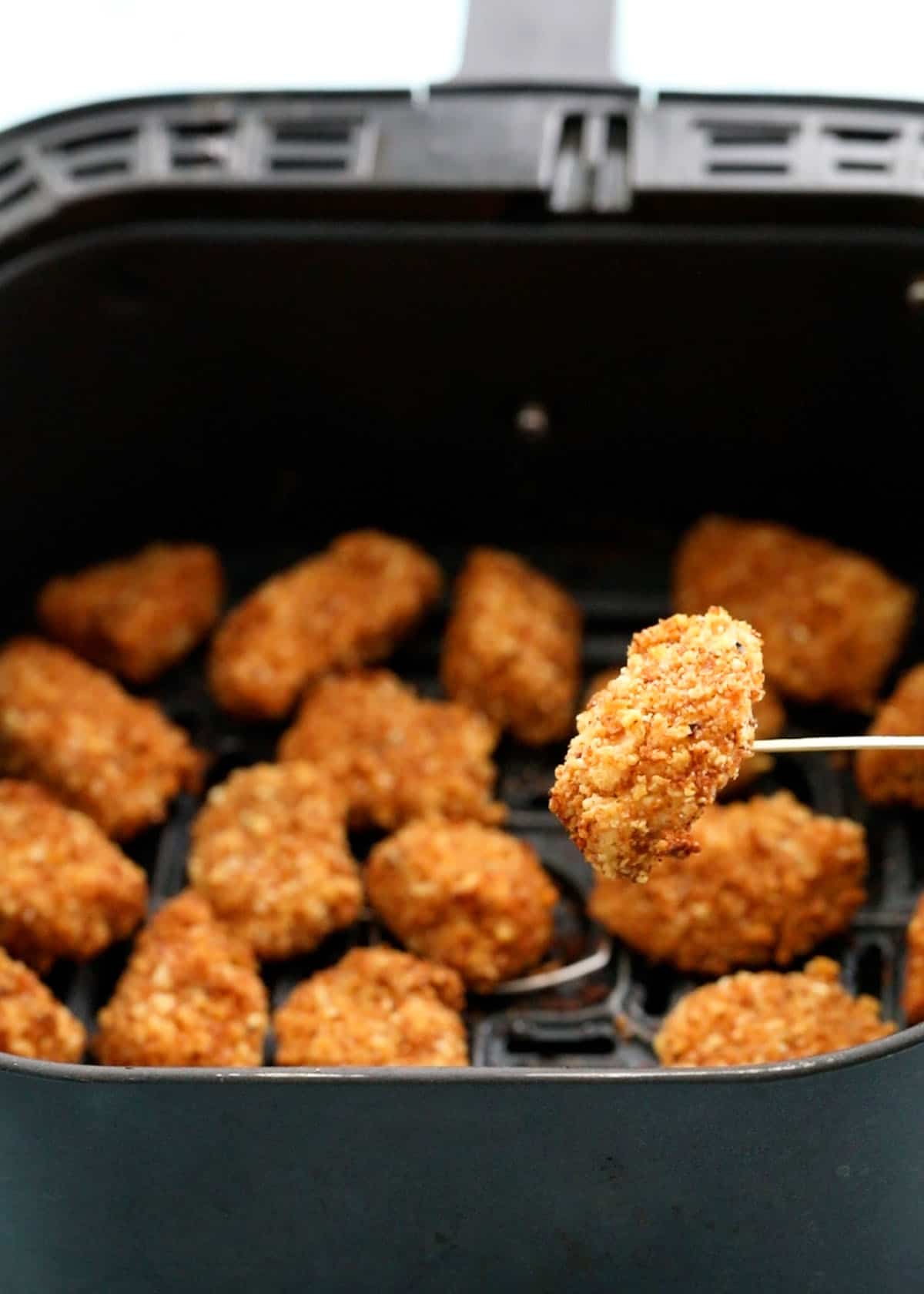 brown chicken nuggets in an air fryer basket.