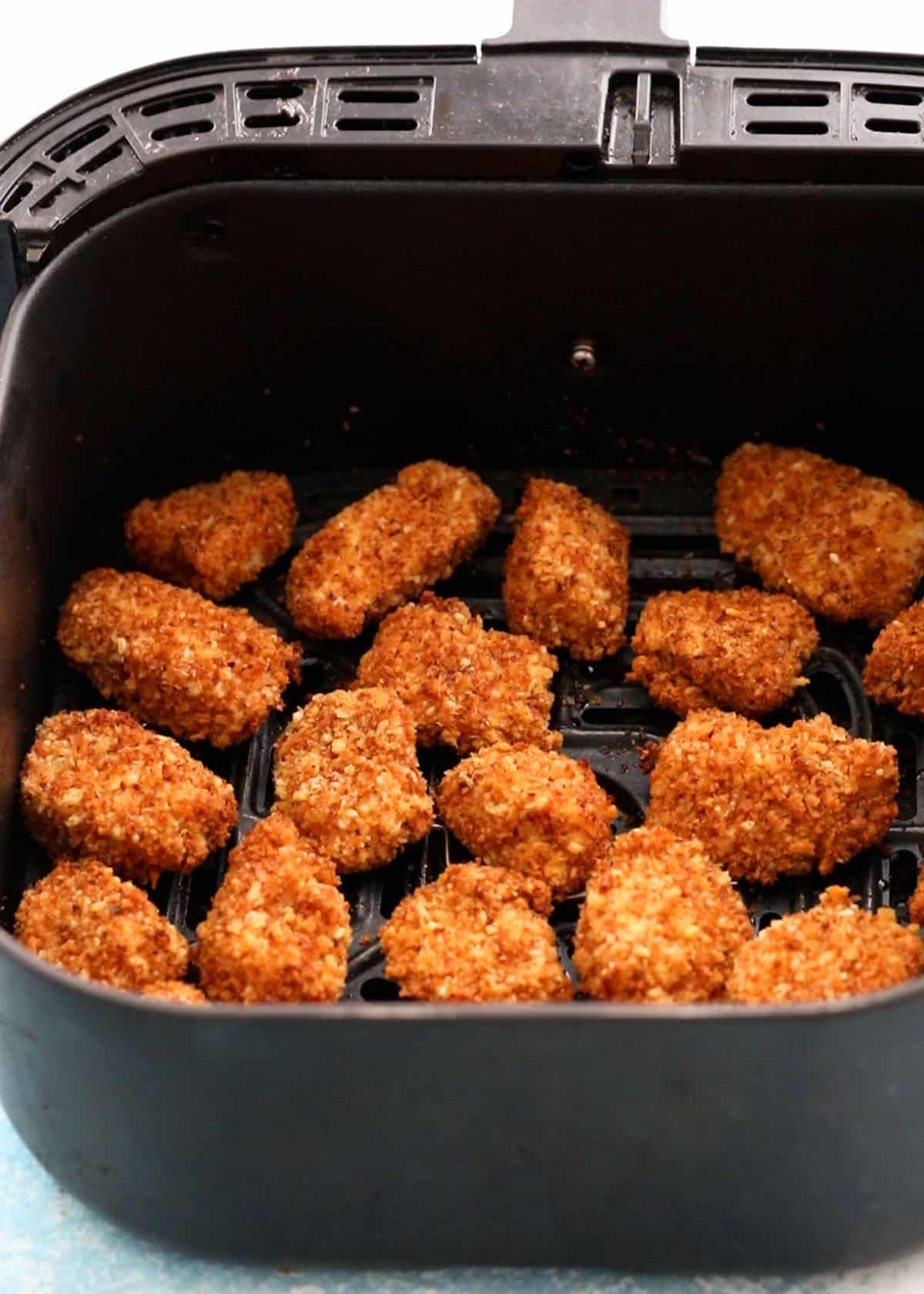 brown chicken nuggets in an air fryer basket.