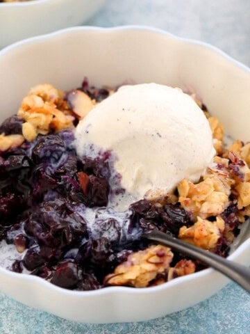 blueberry crisp with one scoop of white vanilla ice cream in a white bowl.