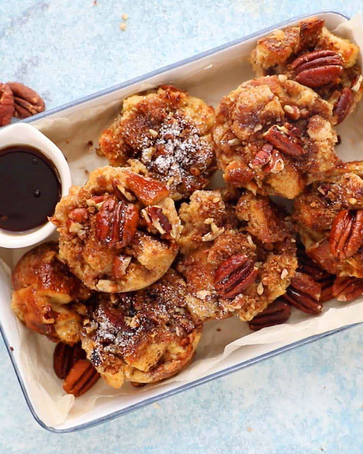 baked french toast cups placed in a white tray along with a small white bowl with maple syrup.