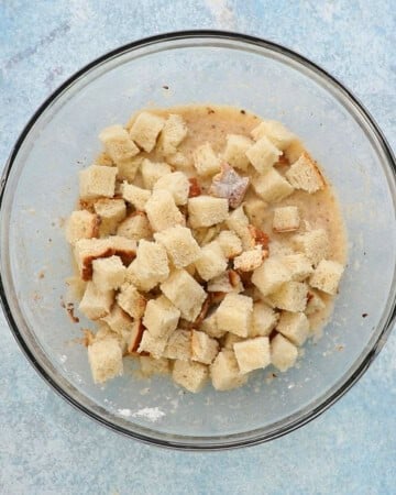 cubed bread placed on top of wet batter in a large glass bowl.