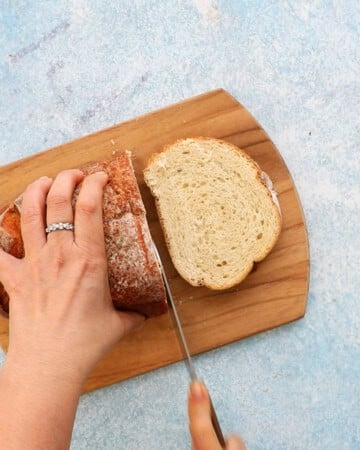 two hands slicing one loaf of bread into slices.