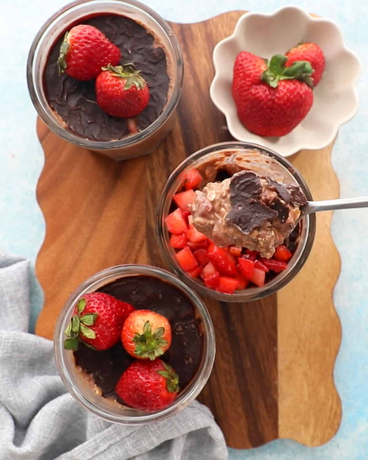 3 glass jars with chocolate strawberry overnight oats on a brown board.