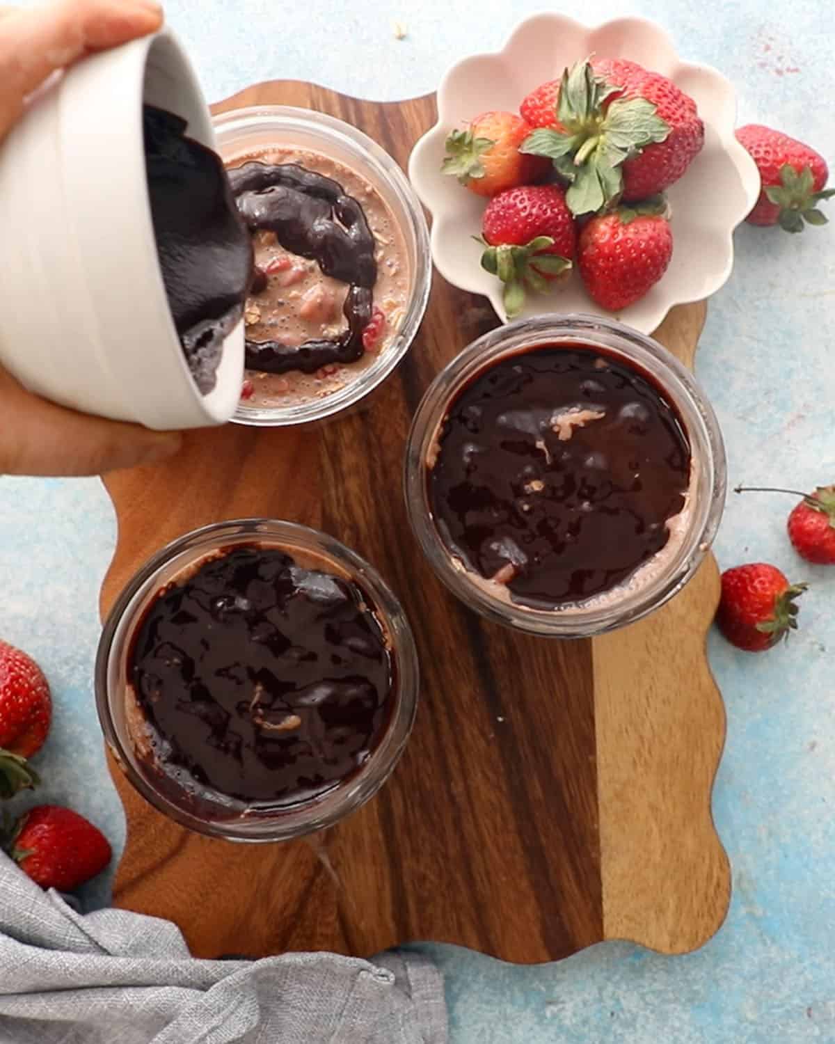 3 glass jars with chocolate strawberry overnight oats on a brown board.