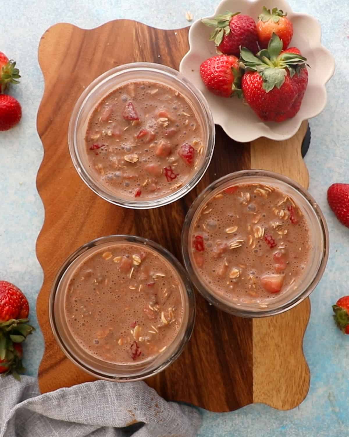 3 glass jars with chocolate strawberry overnight oats on a brown board.