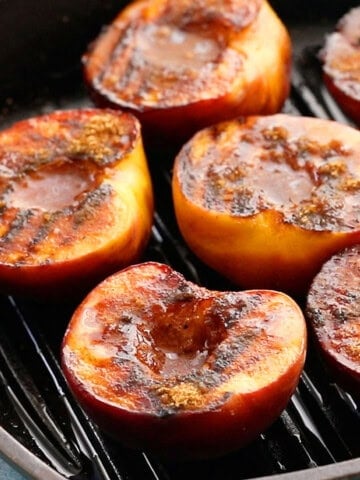 6 grilled peach halves in a black grill pan.