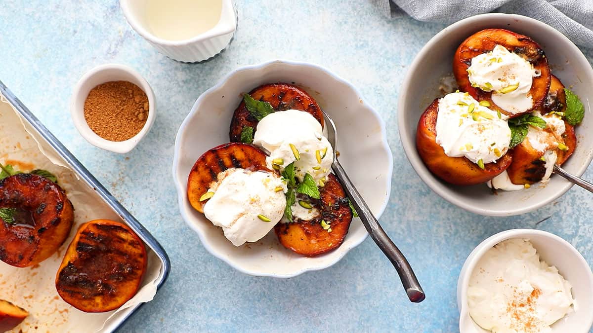 two white bowls with grilled peaches and whipped cream.