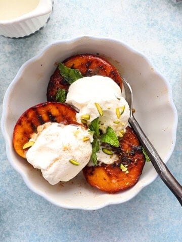 three grilled peach halves topped with whipped cream in a white bowl.