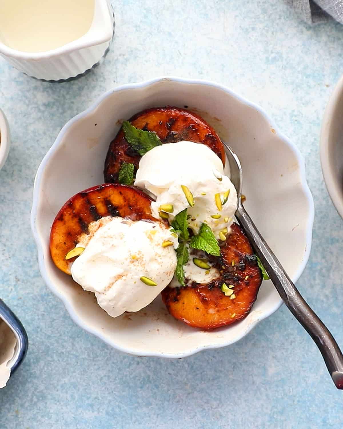 three grilled peach halves topped with whipped cream in a white bowl.